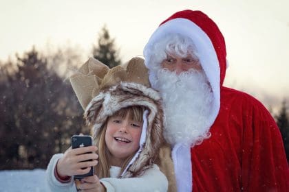 Girl taking selfie with Santa Claus during Christmas celebration.