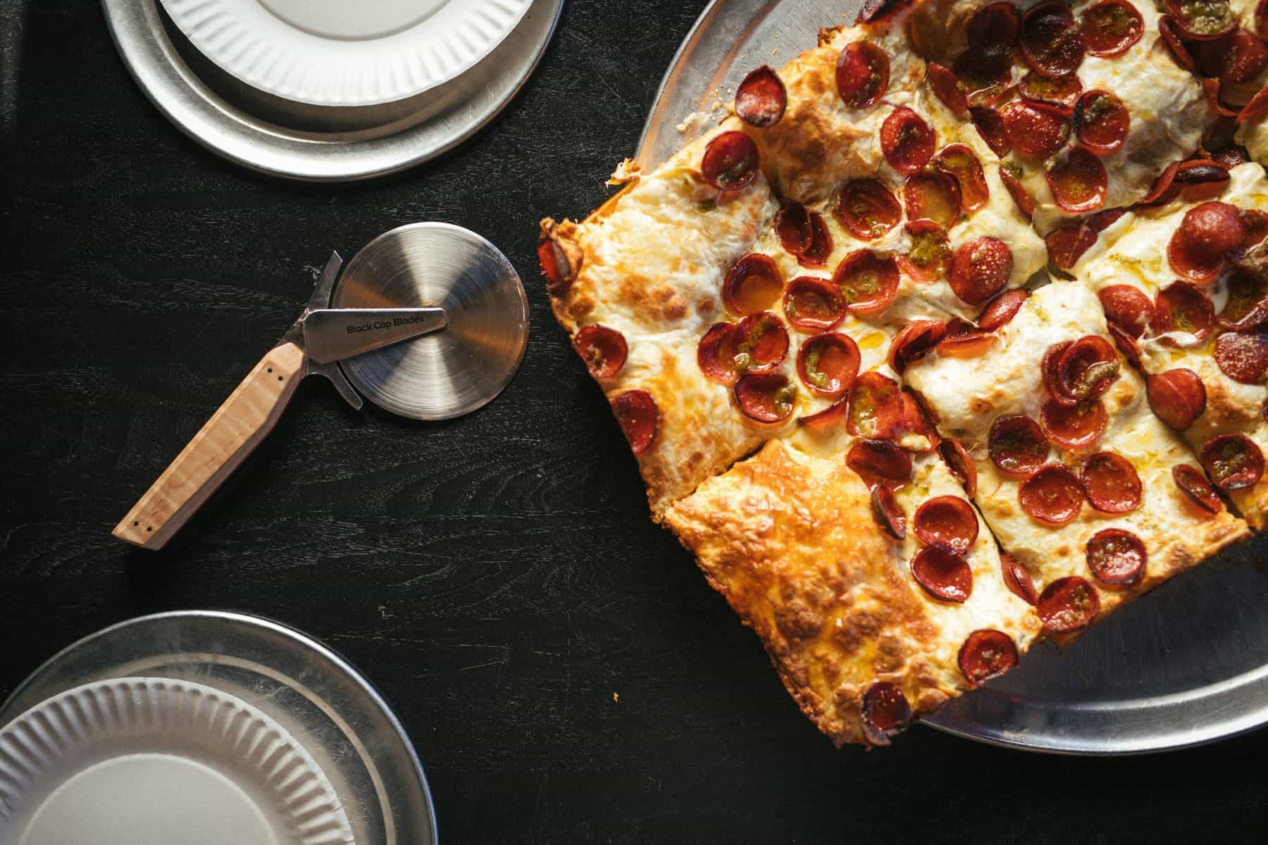 Detroit-style pepperoni pizza on dark table setting.
